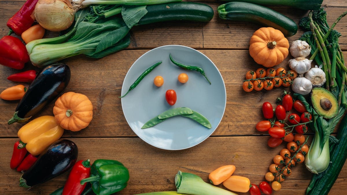 Playful vegetable arrangement creating a sad face on a plate surrounded by fresh produce.