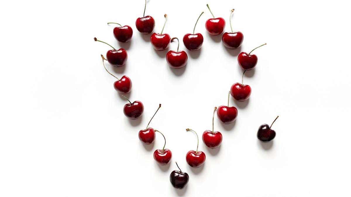Vibrant red cherries arranged in a heart shape on a clean white background, symbolizing freshness and love.